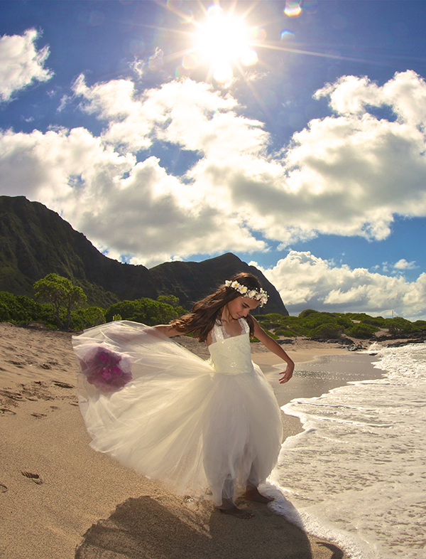 Flower girl in a white dress and flower crown dancing on the shore